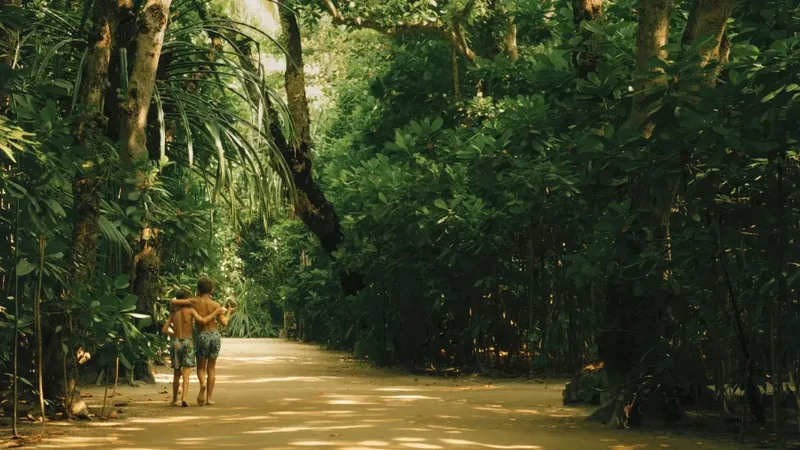 Deux jeunes hommes marchent sur un chemin bordé de végétation tropicale