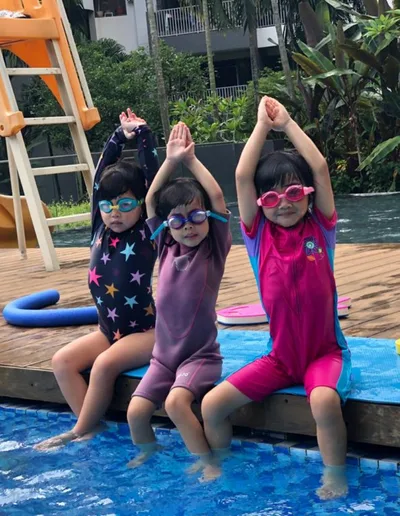 Trois enfants souriants avec lunettes de soleil au bord d'une piscine