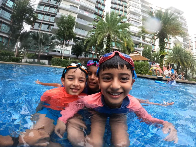 Trois enfants souriants en maillot de bain et lunettes de natation dans une piscine