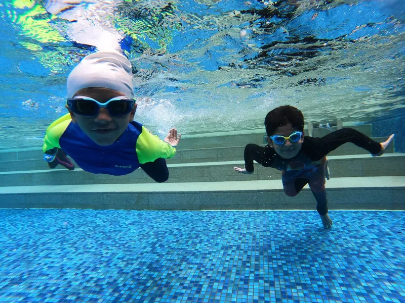 Deux enfants sourient et nagent sous l'eau dans une piscine