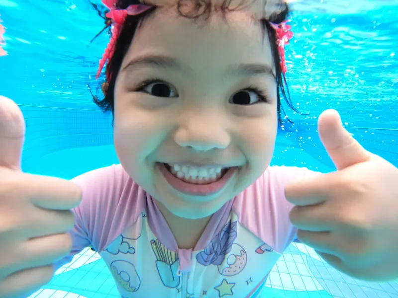 Enfant souriant sous l'eau avec les pouces levés signe d'approbation