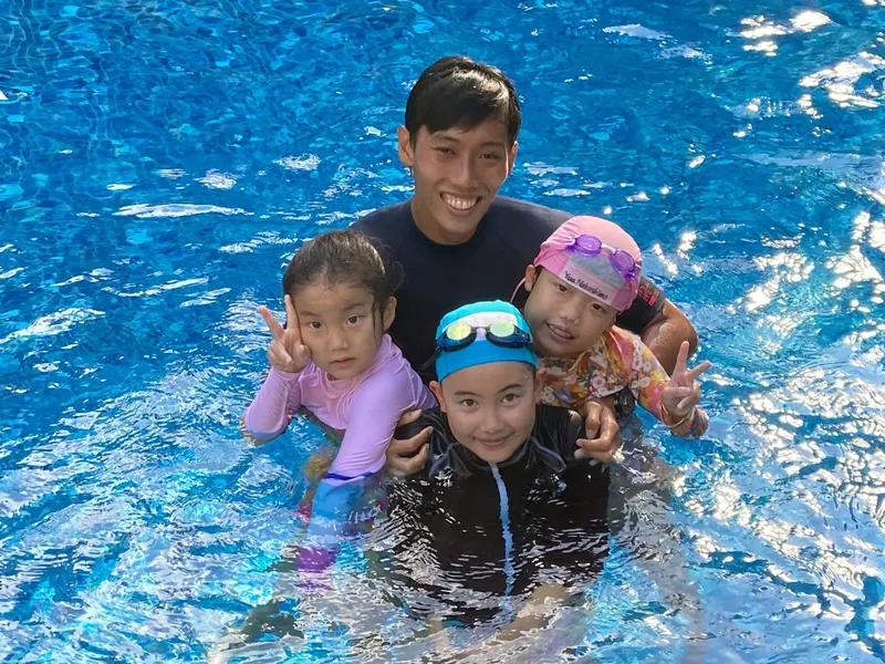 Quatre personnes souriantes dans une piscine, un homme et trois enfants