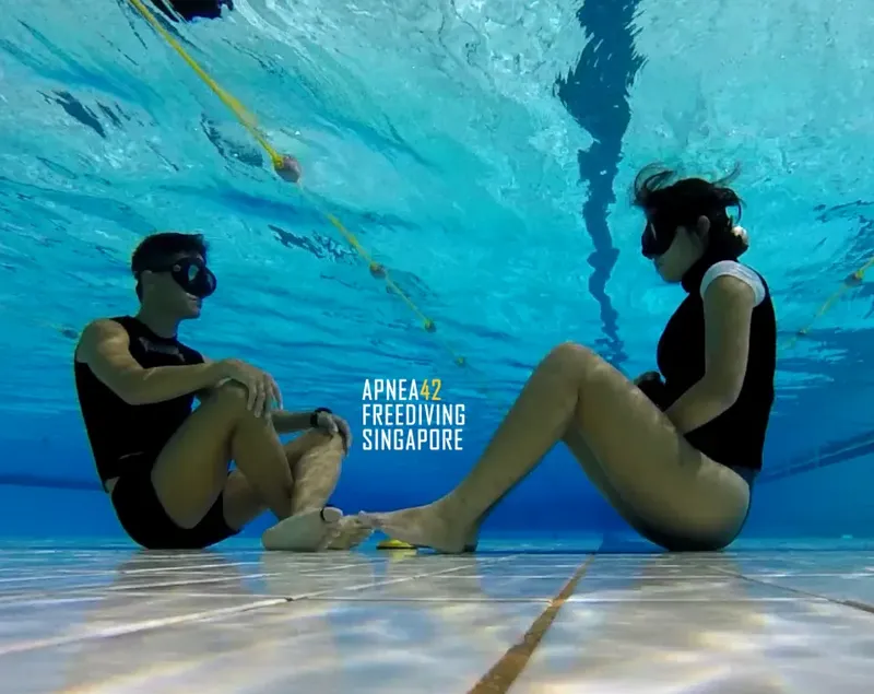 Deux personnes en apnée assises face à face dans une piscine