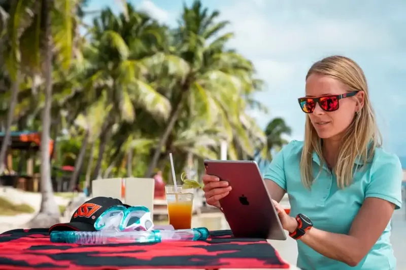 Femme utilisant une tablette sur une plage avec du matériel de plongée