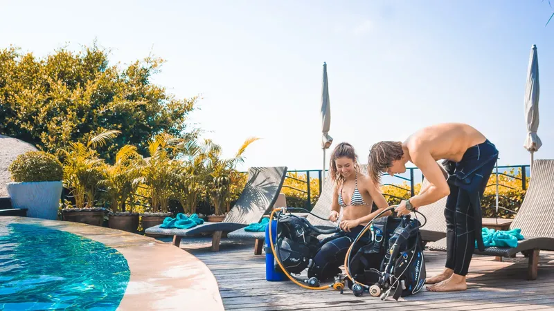Deux plongeurs s'équipent sur une terrasse ensoleillée près d'une piscine