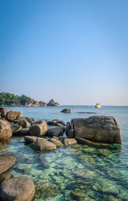 Paysage marin avec des rochers, une plage et un bateau jaune au loin