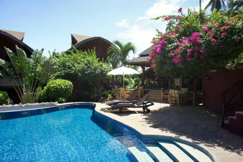 Piscine devant bâtiments colorés, végétation tropicale et mobilier de jardin