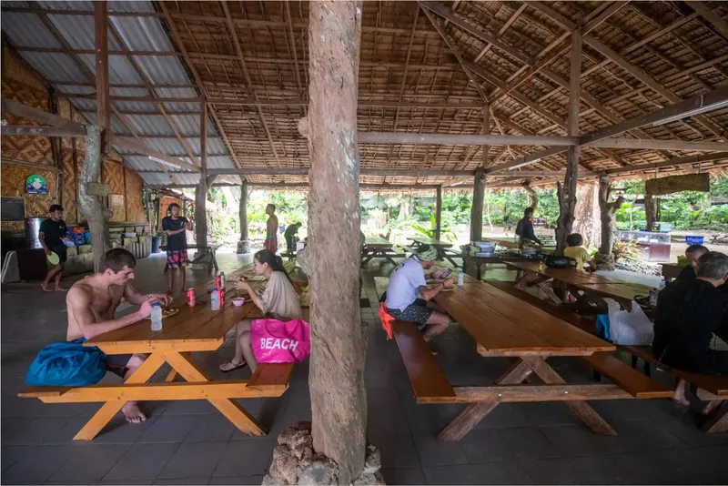 Des personnes mangent et discutent à des tables en bois abritées