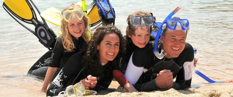 Famille souriante en combinaison de plongée sur une plage ensoleillée