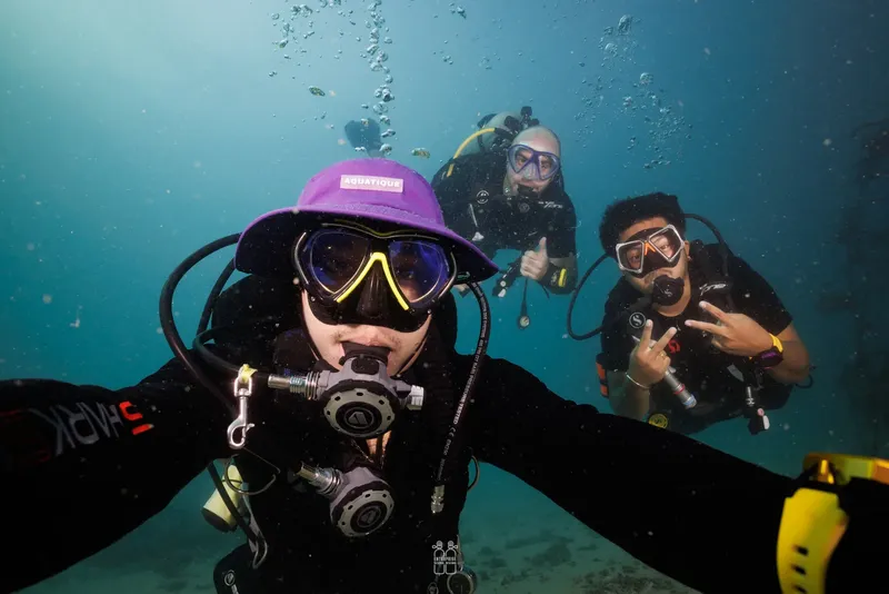 Trois plongeurs souriants font des signes de la main sous l'eau