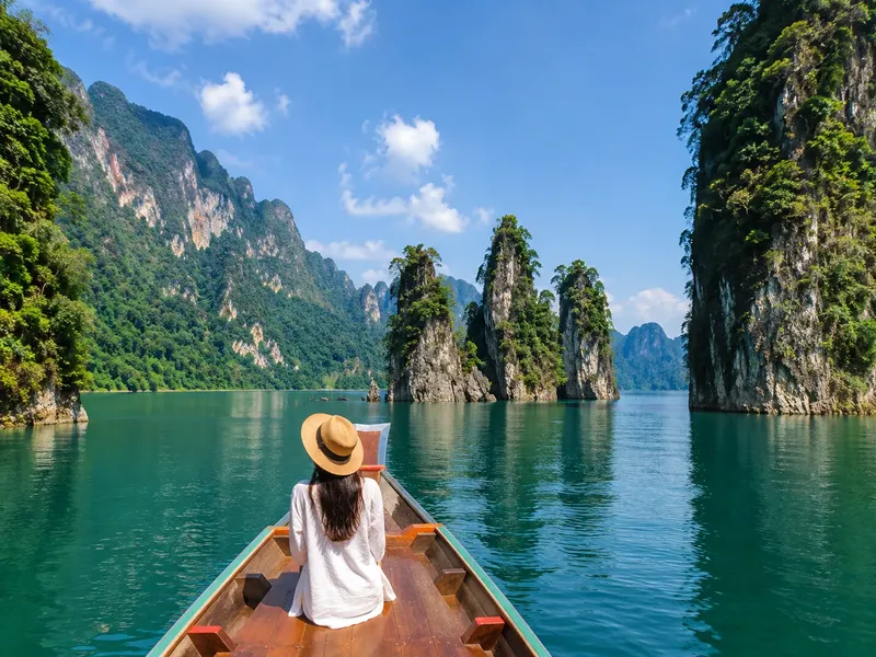 Femme en chapeau sur un bateau, paysage montagneux et eau turquoise