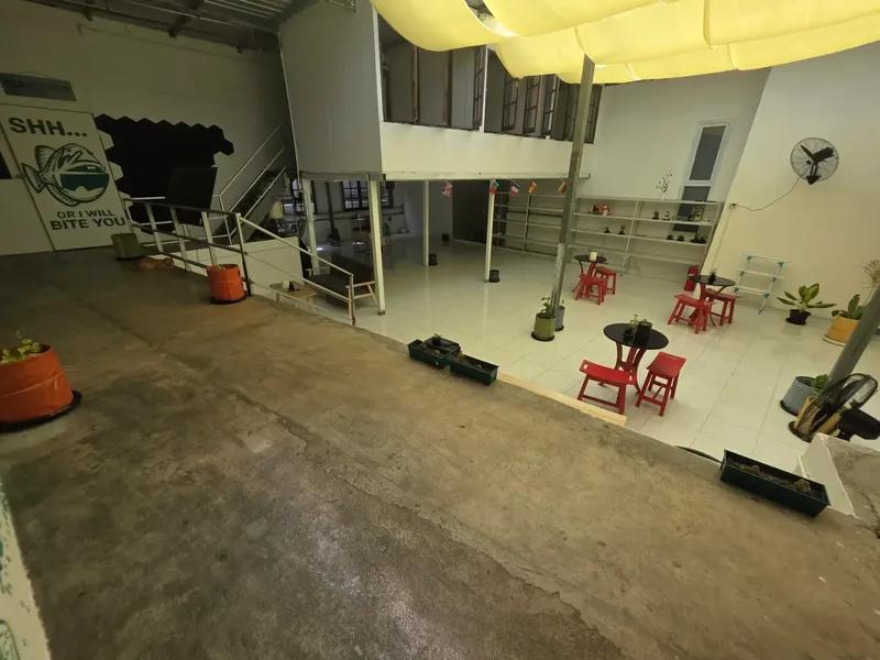 Grande salle ouverte avec tables rouges, plantes et escalier métallique