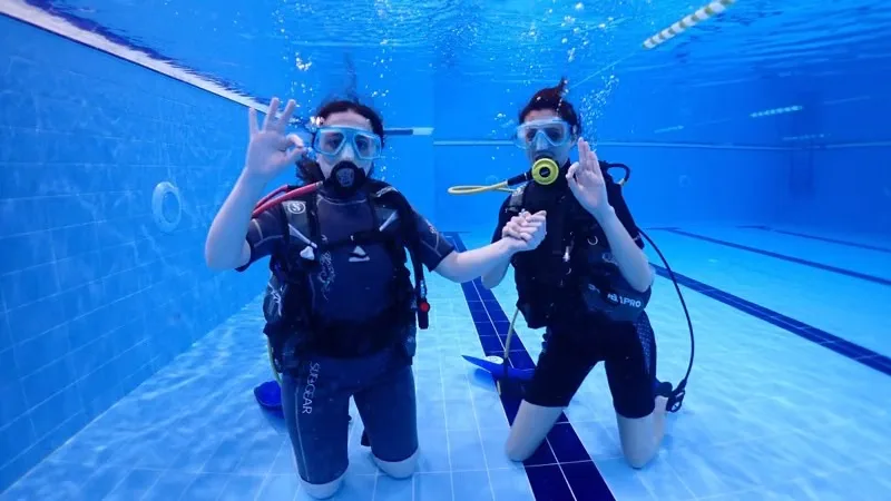 Deux plongeurs souriants en combinaison dans une piscine bleue