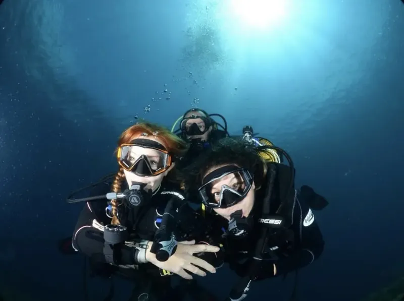 Trois plongeurs souriants en combinaison, masque et détendeur sous l'eau