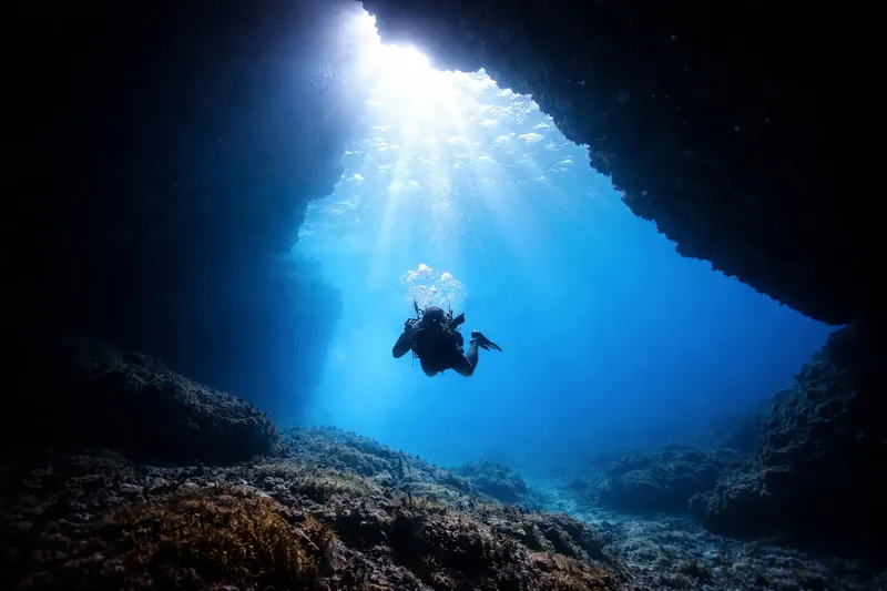 Plongeur explorant une grotte sous-marine éclairée par un rayon de soleil