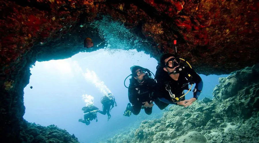 Trois plongeurs explorent une grotte sous-marine avec une lumière vive