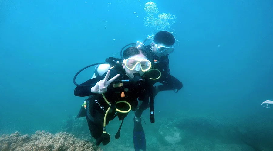 Deux plongeurs souriants font un signe de la main sous l'eau