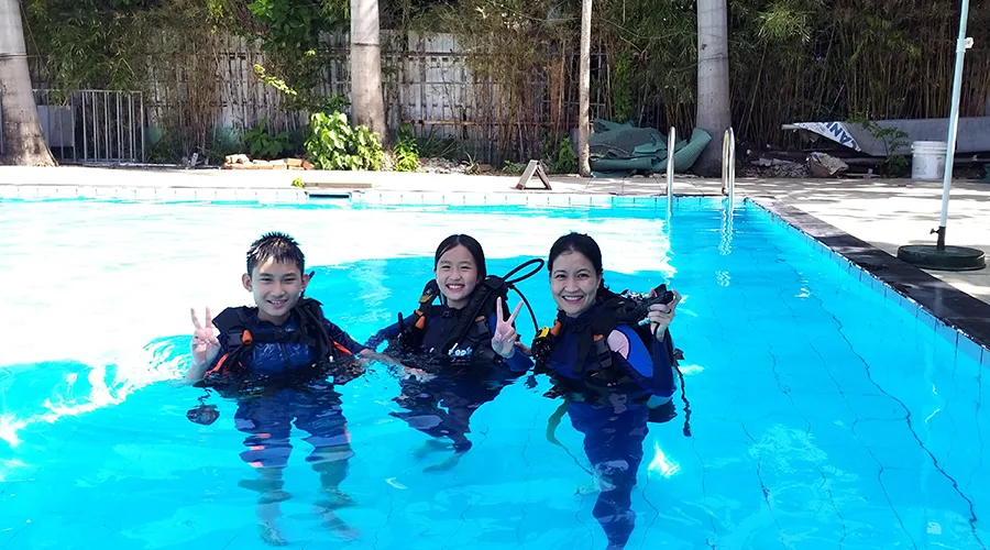 Trois plongeurs souriants en combinaison et gilet dans une piscine