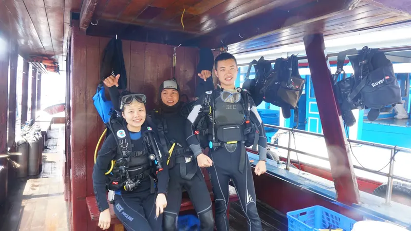 Trois plongeurs équipés sourient à bord d'un bateau de plongée