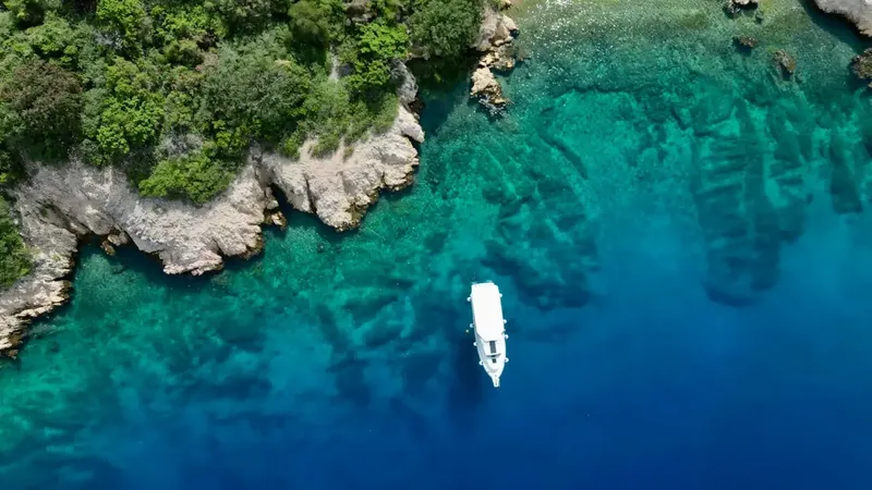 Vue aérienne d'un bateau de plaisance naviguant dans une eau turquoise claire