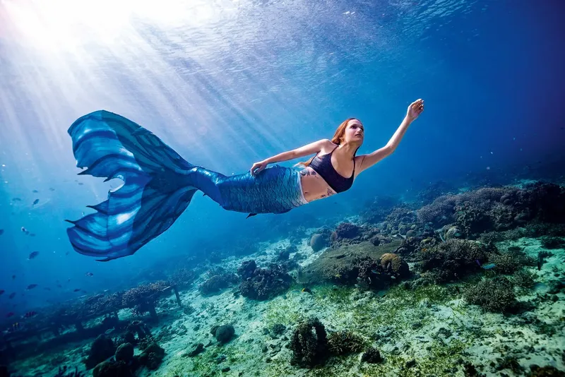Une femme avec une queue de sirène nage sous l'eau avec des rayons de soleil