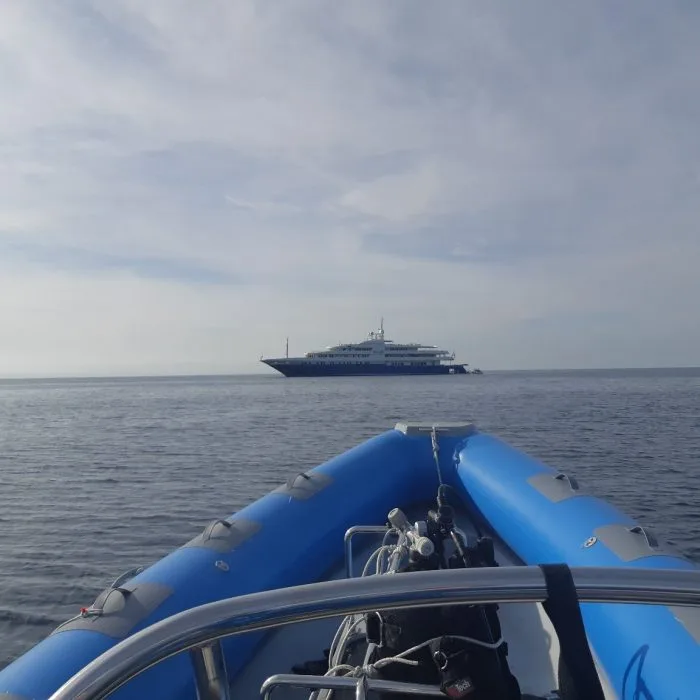 Bateau semi-rigide bleu en mer, grand navire à l'horizon, ciel nuageux