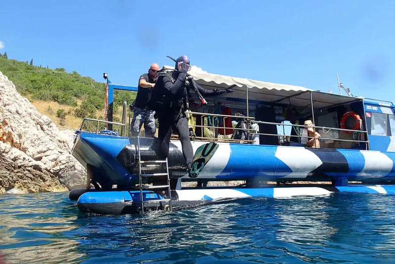 Plongeur en combinaison s'apprête à descendre d'un bateau bleu et blanc