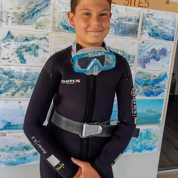 Jeune plongeur souriant en combinaison, masque et détendeur prêt à plonger