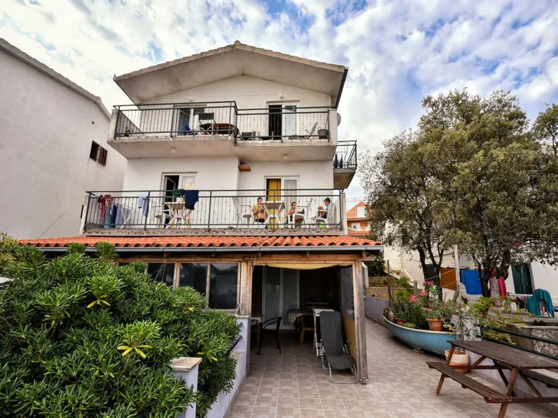 Bâtiment blanc à deux étages avec des balcons et des personnes assises