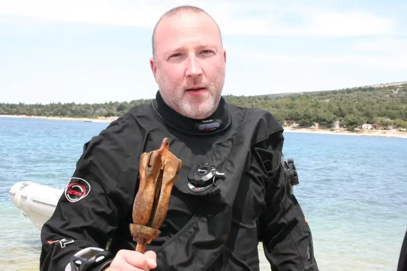 Plongeur tenant une ancienne ancre rouillée sur une plage ensoleillée