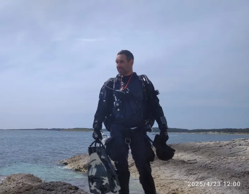 Plongeur en combinaison complète sur un rivage rocheux ensoleillé