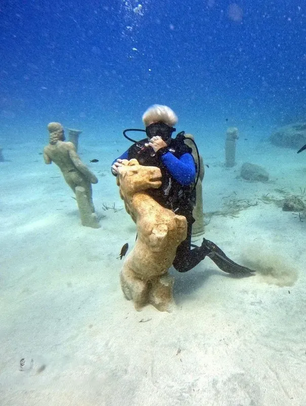Plongeur étreignant une statue sous-marine dans un environnement sablonneux clair