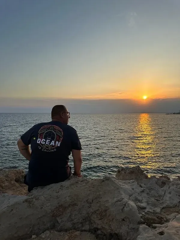 Homme assis sur des rochers, regardant le coucher de soleil sur la mer