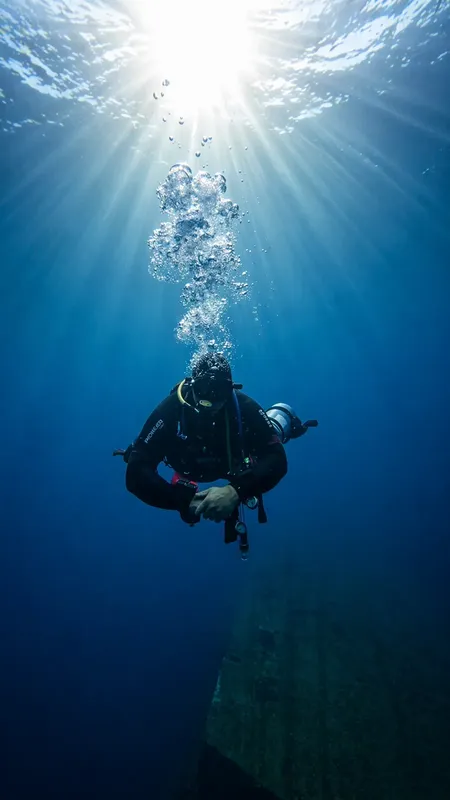 Plongeur en scaphandre noir évolue dans une eau bleue et lumineuse