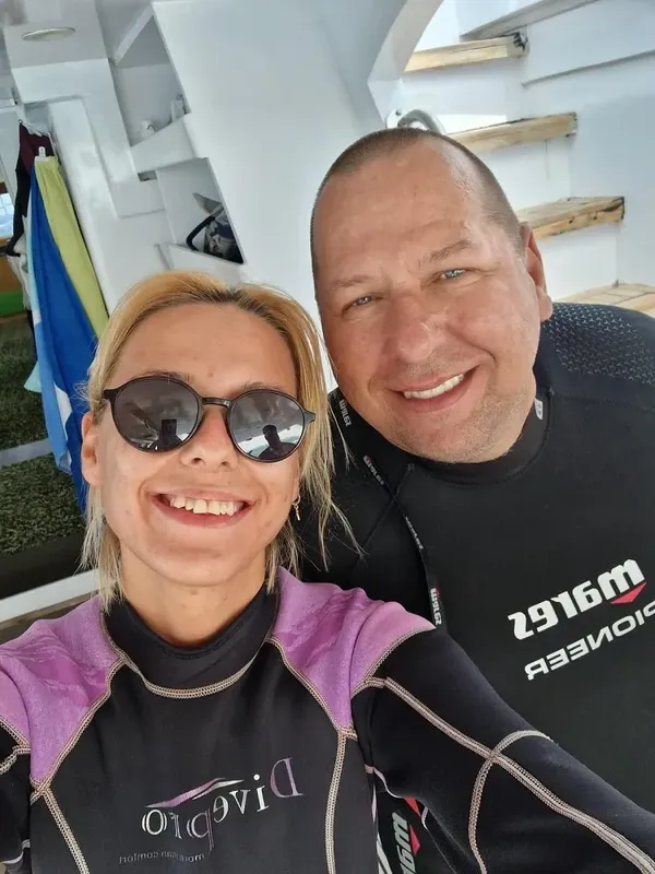 Deux personnes souriantes en combinaison de plongée sur un bateau