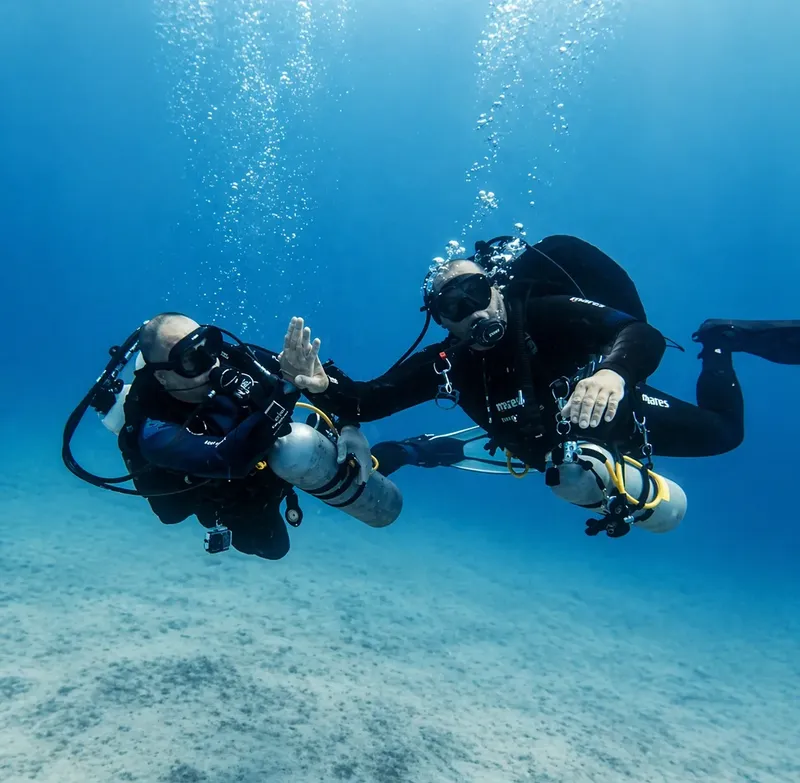 Deux plongeurs en combinaison communiquent sous l'eau dans un environnement bleu