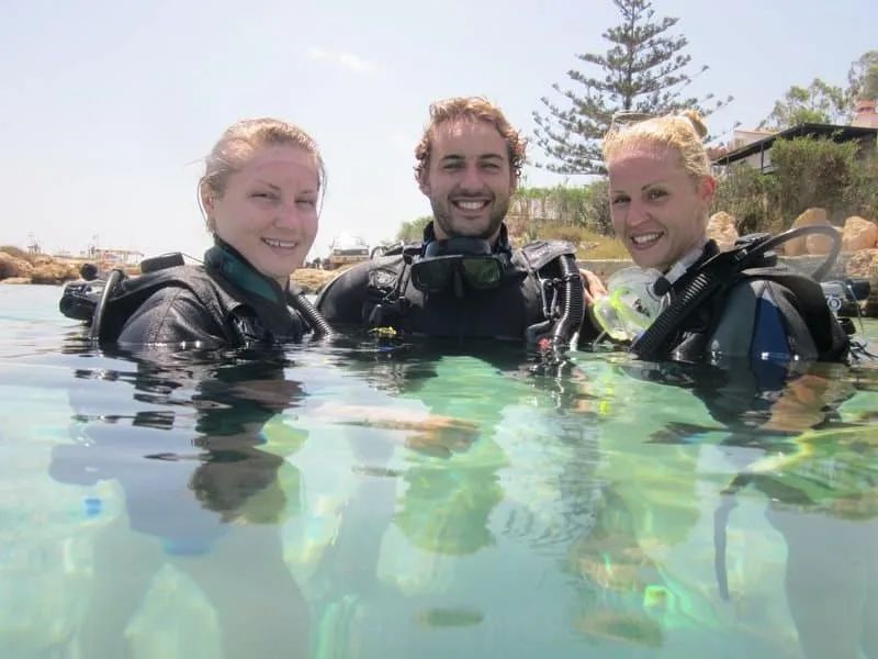 Trois plongeurs souriants, équipés, émergent dans une eau turquoise claire