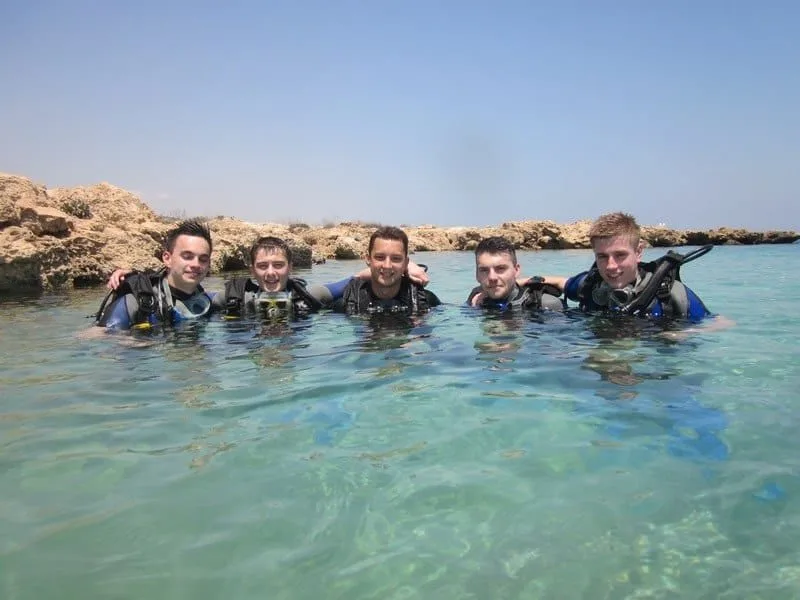 Cinq plongeurs souriants dans une eau turquoise peu profonde