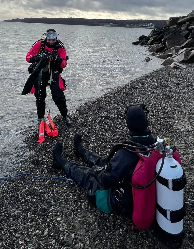 Deux plongeurs sur une plage de galets se préparent à plonger