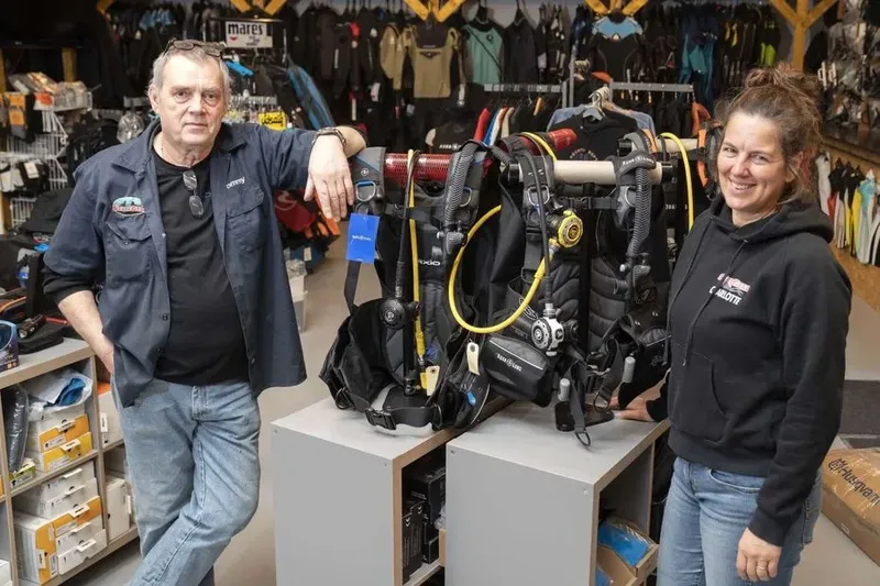 Deux personnes souriantes se tiennent de part et d'autre d'un équipement de plongée