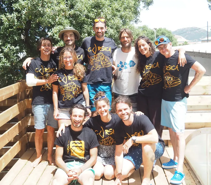 Groupe de personnes souriantes posant ensemble en extérieur, portant des t-shirts