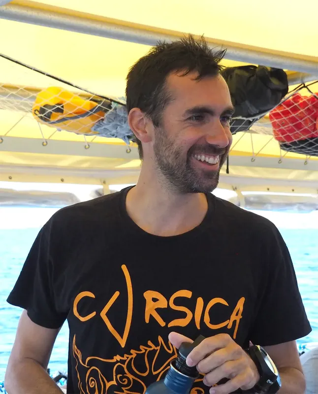 Un homme souriant porte un t-shirt avec le mot Corse et plonge