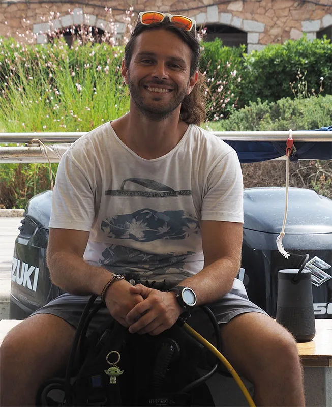 Un homme souriant, portant un équipement de plongée, assis à quai