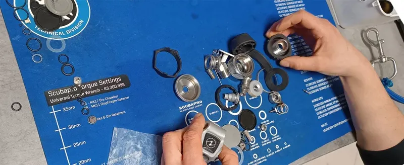 Mains manipulant des pièces de détendeur de plongée sur un tapis bleu