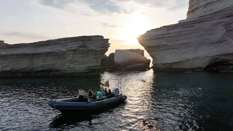 Bateau de plongee naviguant entre des falaises rocheuses au coucher du soleil