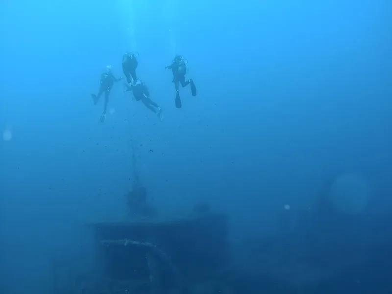 Trois plongeurs explorent une épave sous-marine dans l'eau bleue