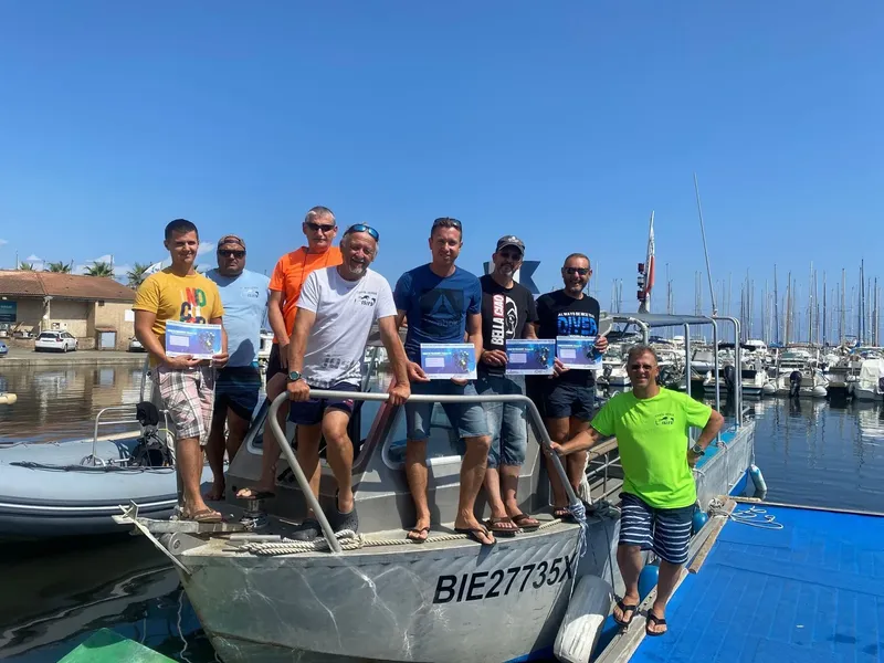 Groupe de plongeurs souriants posant sur la proue d'un bateau gris
