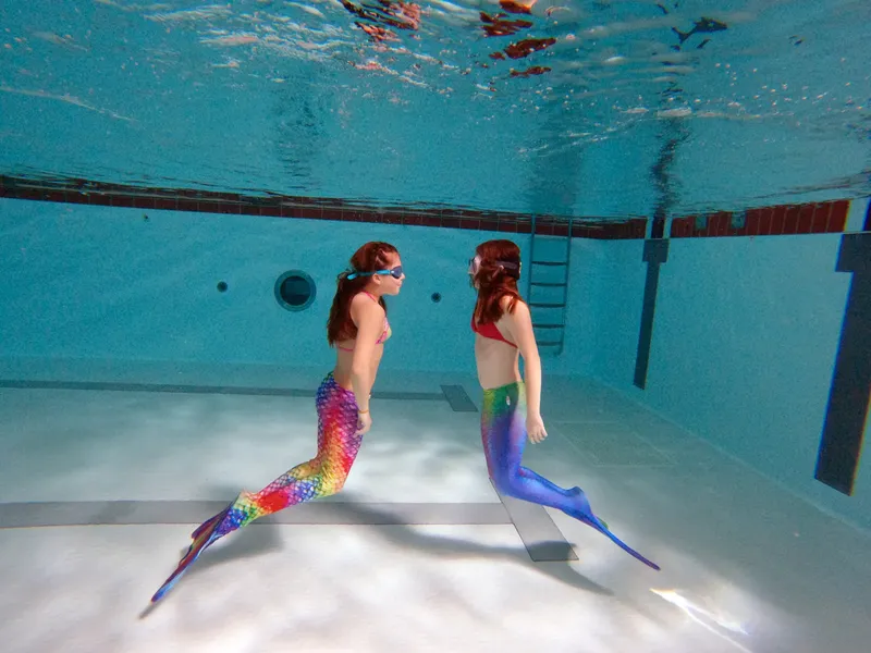 Deux femmes en sirène nagent sous l'eau dans une piscine