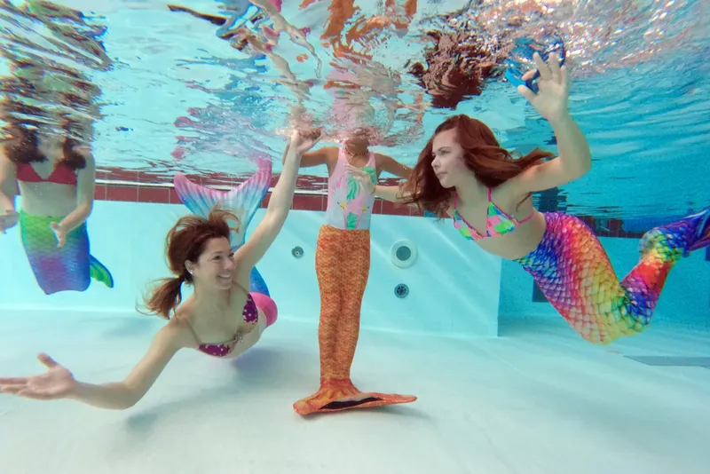 Trois jeunes femmes sourient et nagent sous l'eau avec des queues de sirène