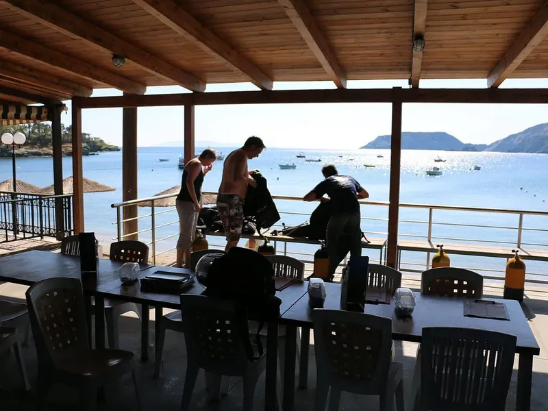 Terrasse ombragée avec plongeurs préparant leur matériel face à la mer